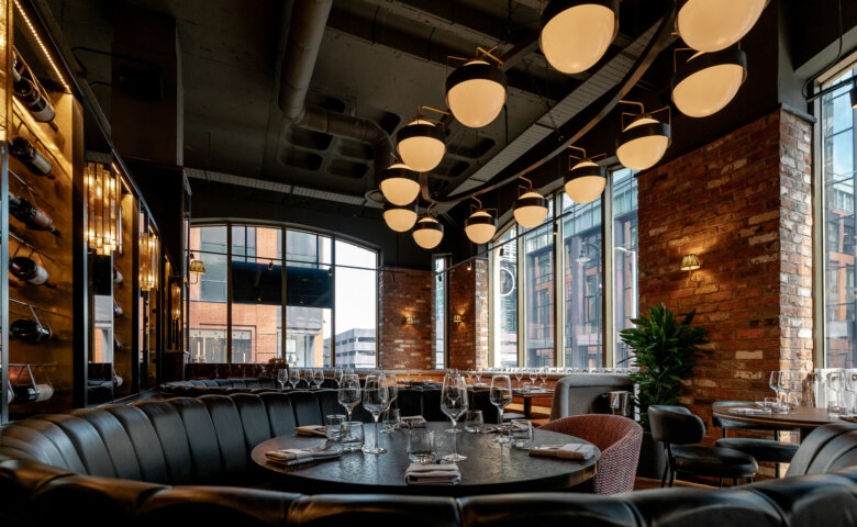 View of Birmingham's Pasture steakhouse restaurant dining room, with leather seating and bespoke brass oval lighting system with opal glass globes